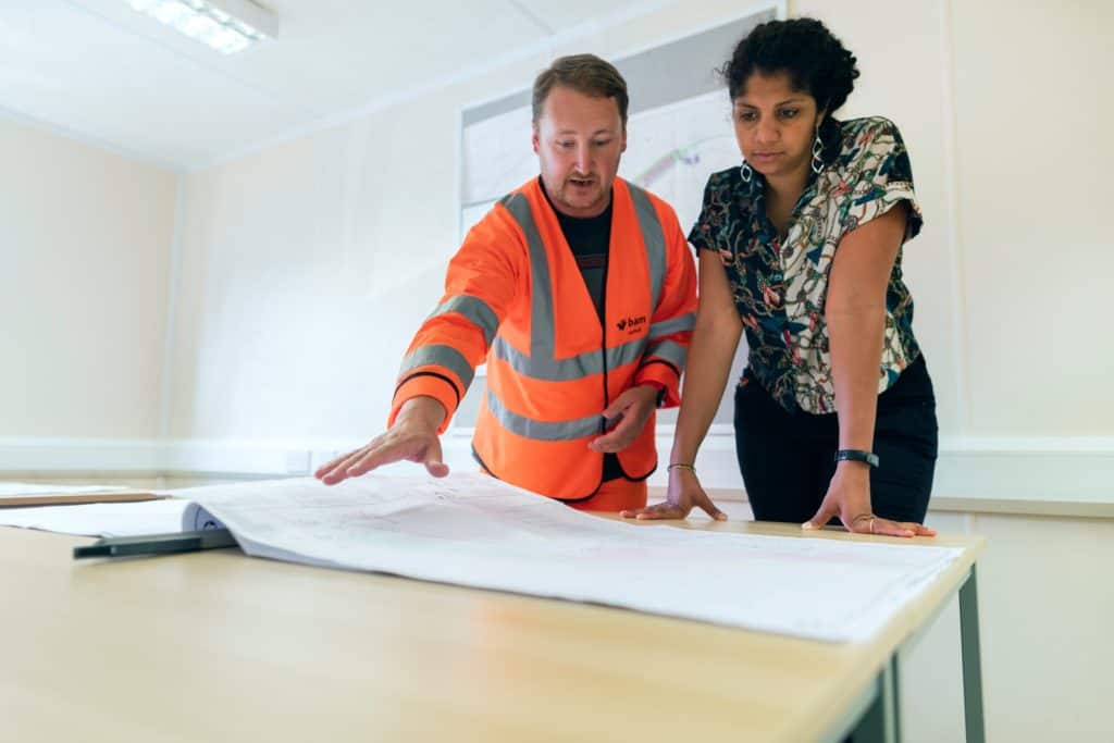 two engineers stand over large paper manufacturing plans